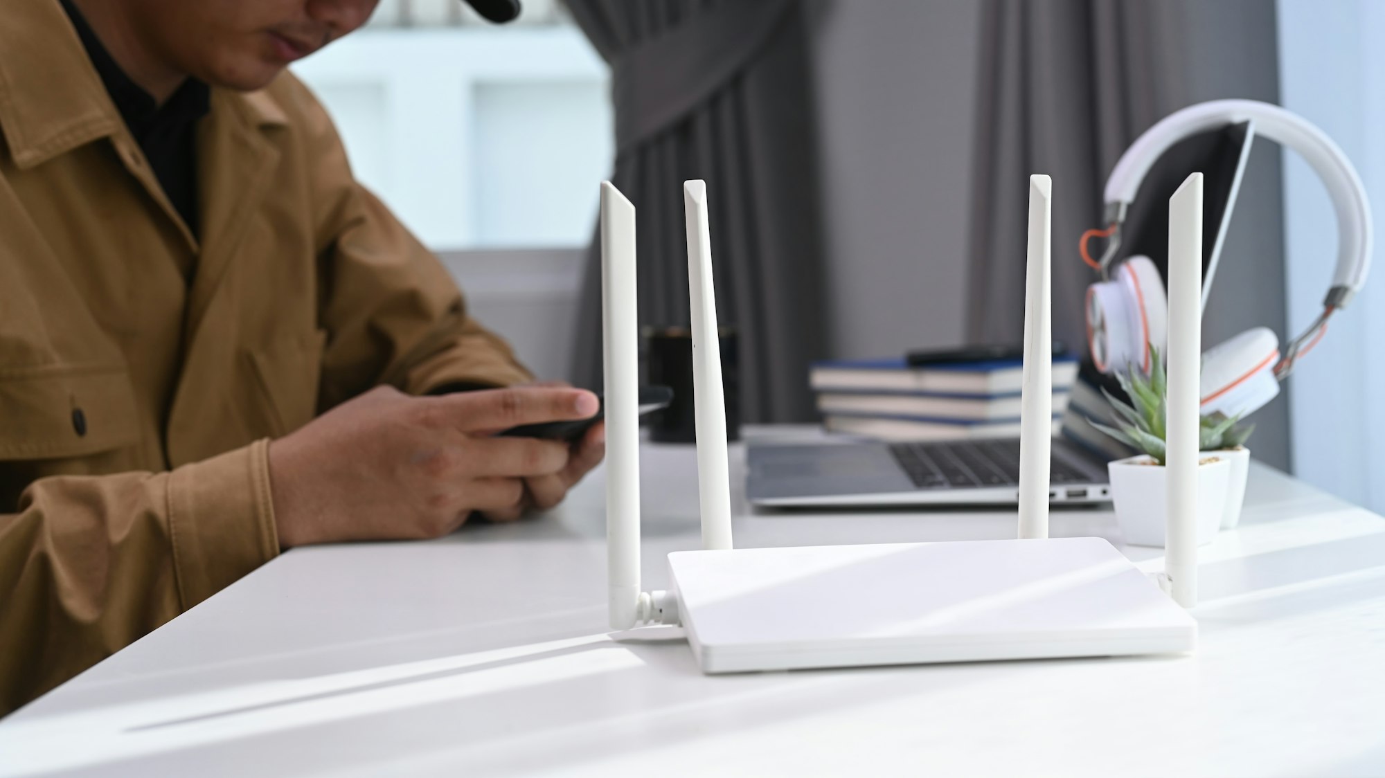 Closeup view of a wireless router with businessman using laptop and smartphone in home office.